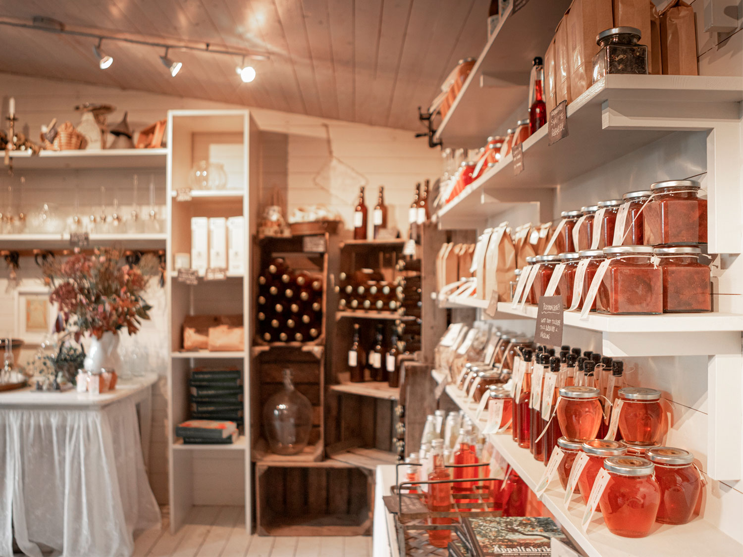 Inne i butiken finns vita hyllor fyllda med glasflaskor och glasburkar med marmelader och saft