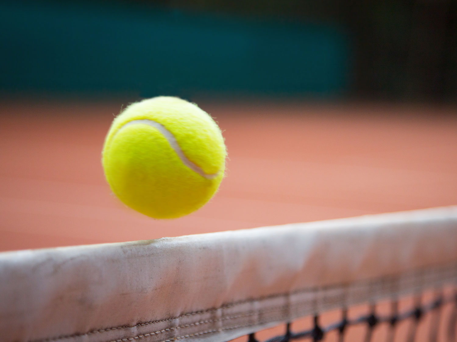 En gul tennisboll flyger över ett nät
