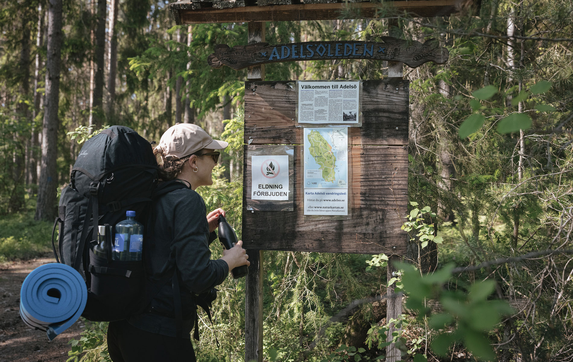 En kvinna med ryggsäck på ryggen står och tittar på en informationstavla i skogen.