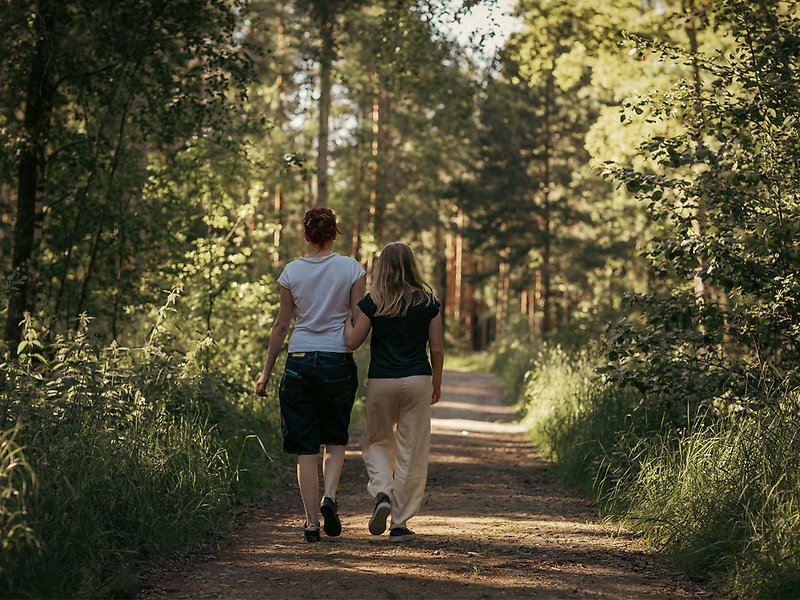 Två tjejer går arm i arm på en bred stig genom en skog