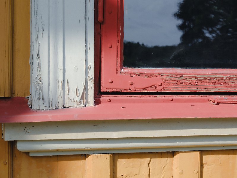 Närbild på rött fönster med vitt fönsterfoder och gul träfasad