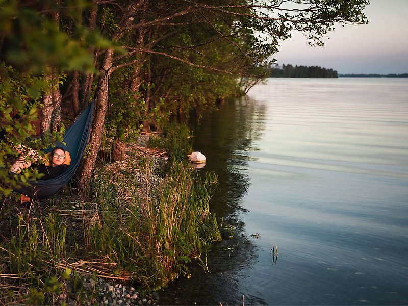 Tälta Ekerö: En tjej ligger i en hängmatta intill vattnet. 