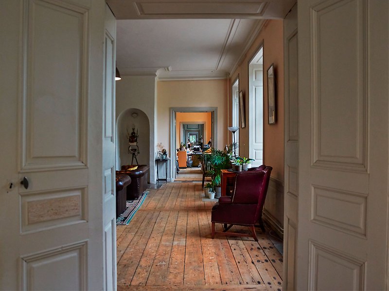 Svartsjö slott - Flera rum ligger i fil. I förgrund syns gråmålade dörrar, trägolv, en fåtölj.