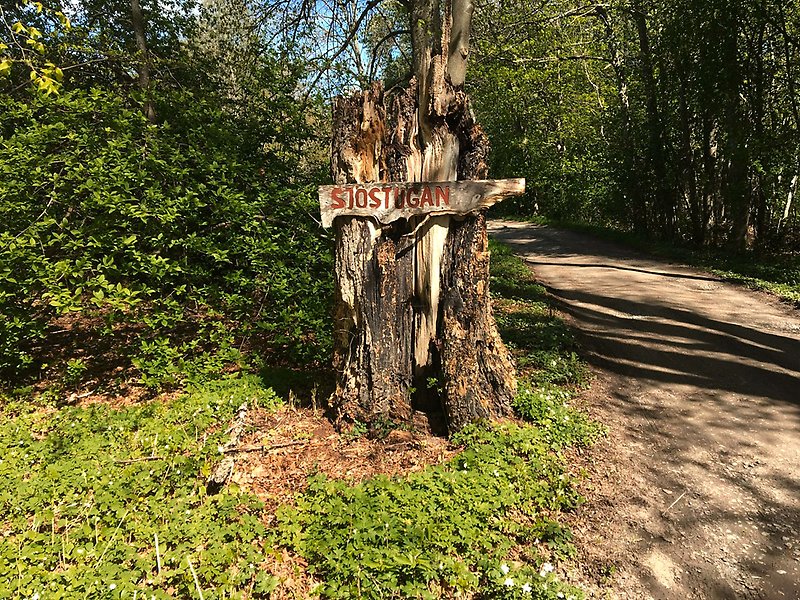 En trädstam med en handmålad skylt där det står Sjöstugan.