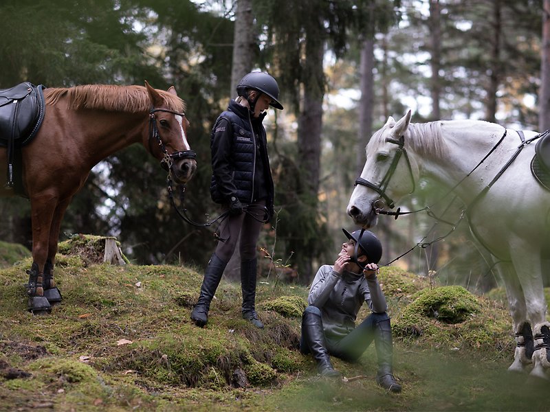 Två flickor håller i en varsin häst och sitter i skogen