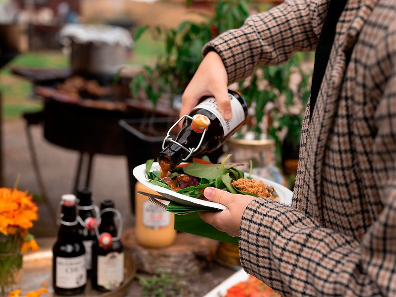 En person håller i en tallrik med mat och heller dressing över salladen.