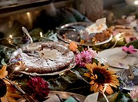 En kaka med pudersocker ligger på en tallrik. Runtom kakan syns solrosor och andra blommor.